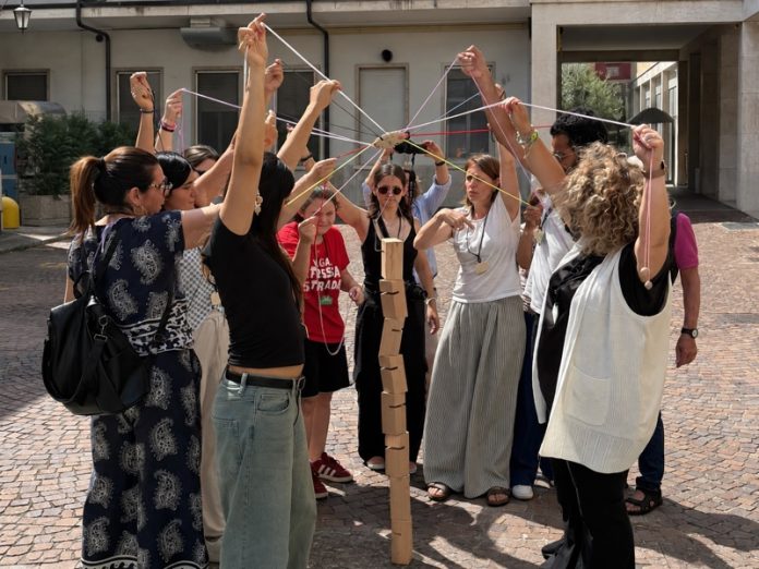 Un gruppo partecipa a un gioco cooperativo con corde e una torre di legno durante la festa dei volontari del Palazzolo.