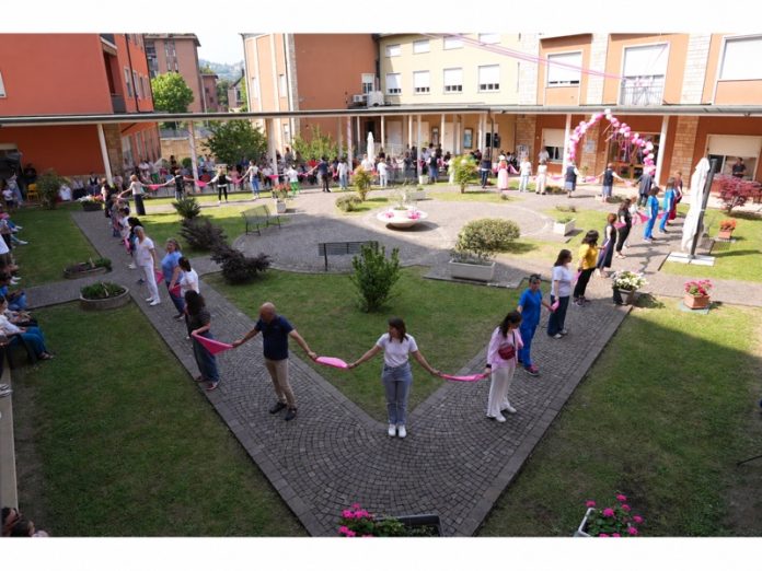 Partecipanti alla festa del Villaggio Teresa Gabrieli disposti in cerchio nel cortile, uniti da foulard rosa.